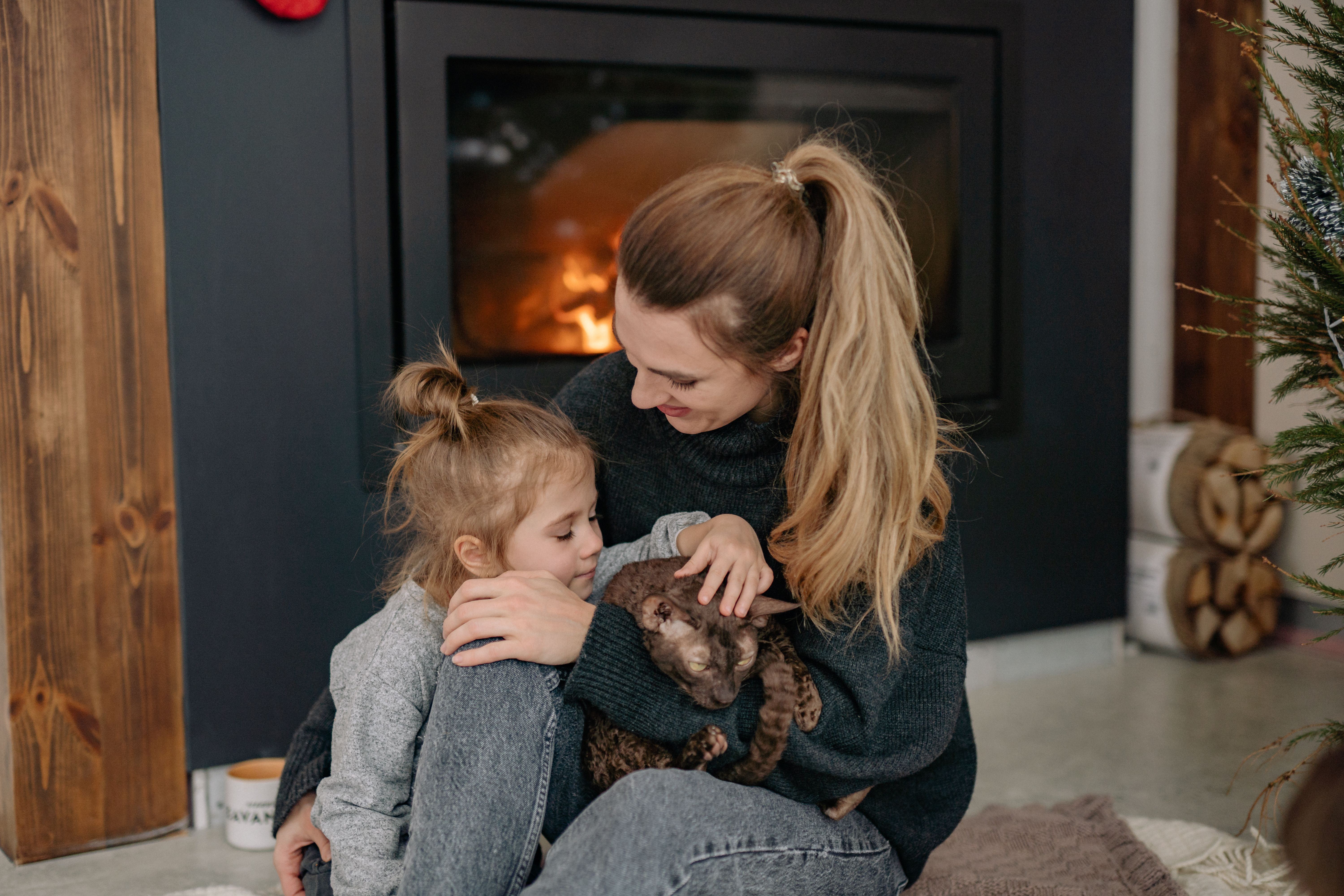 A mother and daughter with their cat by the fireplace